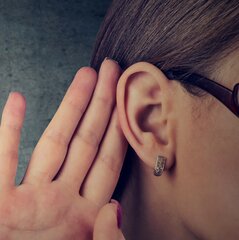 Eine Person hält sich die Hand hinters Ohr und hört aufmerksam zu.