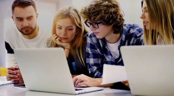 Drei Studierende, die gemeinsam auf ein Laptop schauen und arbeiten.