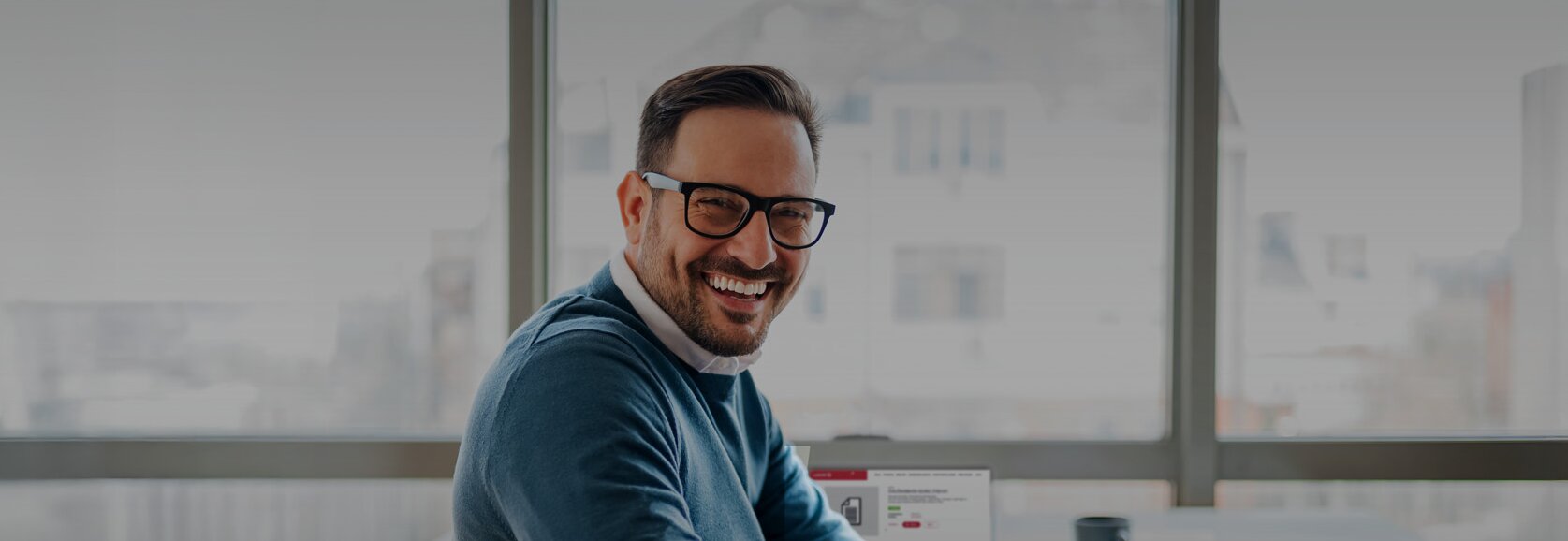 A man sits smiling in front of a laptop on which the Austrian Standards website is displayed.