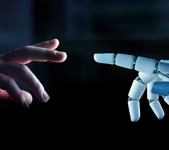 Eine Roboterhand zeigt mit dem Zeigefinger auf die leicht geöffnete Hand eines Menschen.