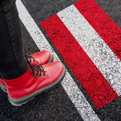 Frau mit roten Schuhen steht am Asphalt mit einer Österreich-Flagge.