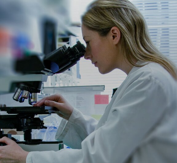 Eine Forscherin blickt in ein Mikroskop und analysiert eine Probe.