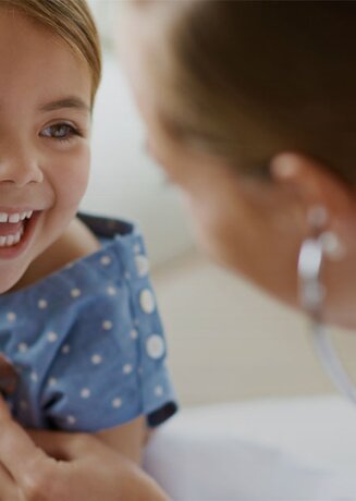Ein junges Mädchen, das von einer Ärztin untersucht wird und dabei ein strahlendes Lächeln zeigt.
